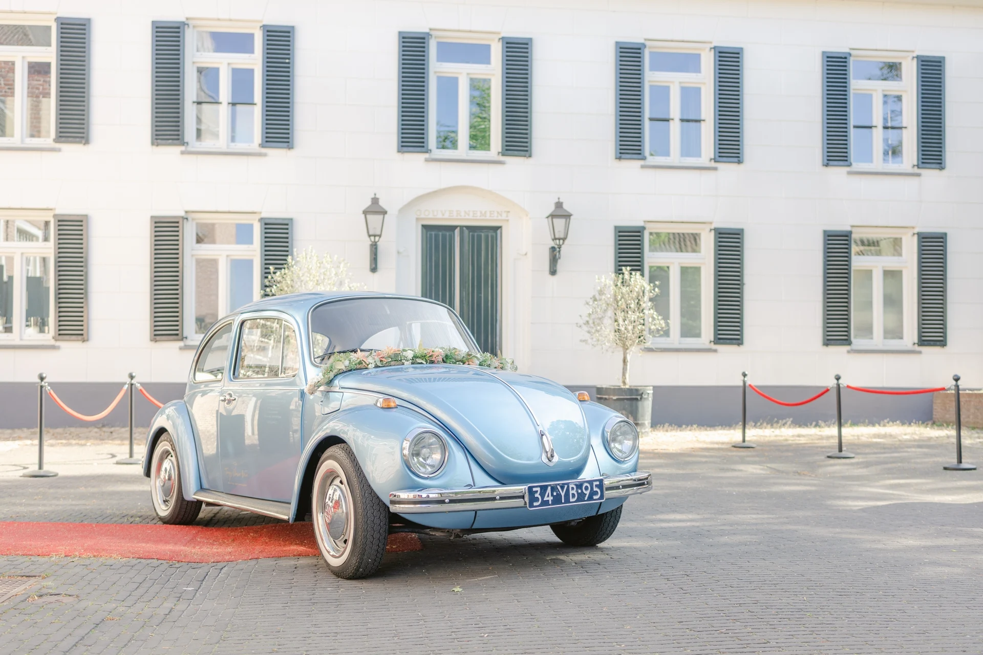 Blauwe trouwauto met bloemen voor wit gebouw